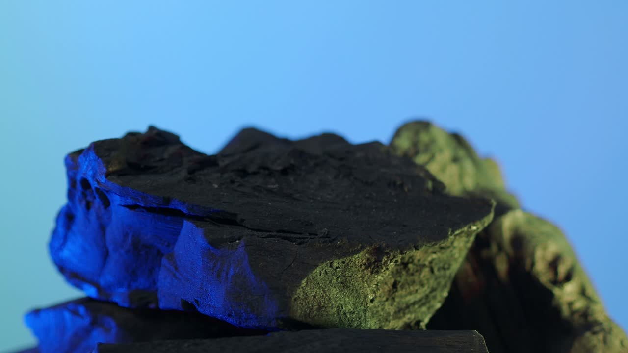 черный уголь. натуральная древесина или традиционный уголь движущаяся петля на синем фоне. съемка на статической камере. 4k с синим и зеленым светодиодным освещением. уголь для приготовления пищи. концепция еды.