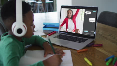 schoolboy using laptop for online lesson at home, with school friend and web chat on screen