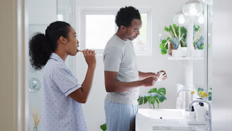 couple wearing pyjamas standing in bathroom at sink brushing teeth in the morning