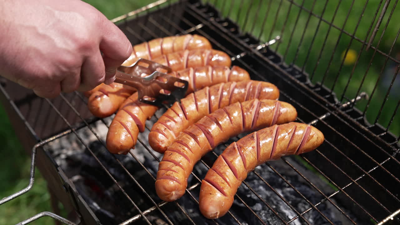 Cooking sausages in smoke outdoors. Tasty roast food on charcoal for picnic. Chef cooking grilled beef hot dog sausage on grill. Close-up.