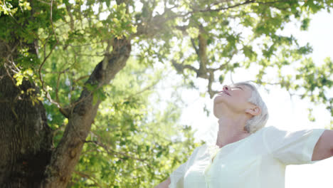 senior woman standing with arms outstretched in the park