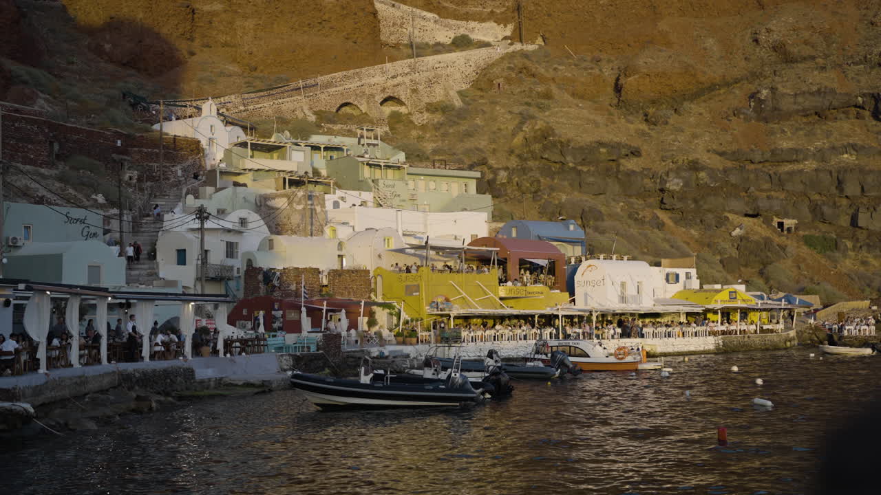 Slow revealing shot of the sun setting over busy restaurants in Santorini