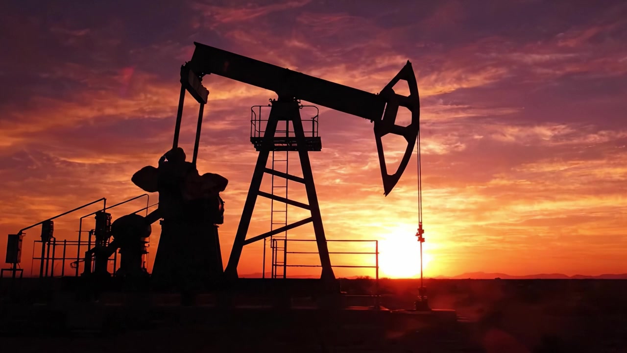 A breathtaking view of an oil pump silhouetted against a vibrant sunset, showcasing the contrast between industrial energy production and the beauty of nature in the evening sky.