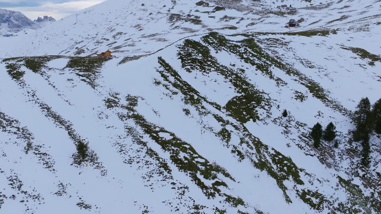 Aerial footage of a snowy hillside with a house that pans up to reveal a mountain peak.