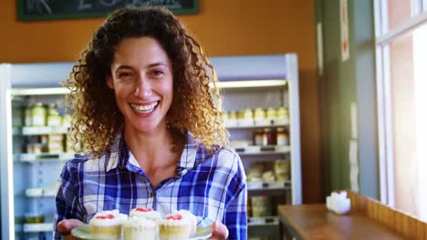 retrato de una mujer sonriente sosteniendo un plato de pastel de taza en un supermercado