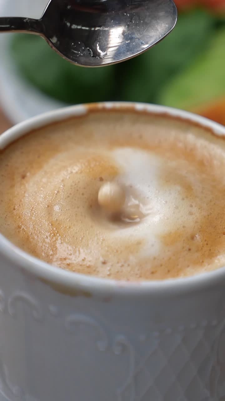 Movimento rallentato di un cubetto di zucchero che cade nel caffè schiumoso