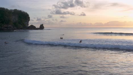 Silhouetted-surfers-catching-waves-at-sunset-on-Padang-Padang-Beach,-Bali,-Indonesia