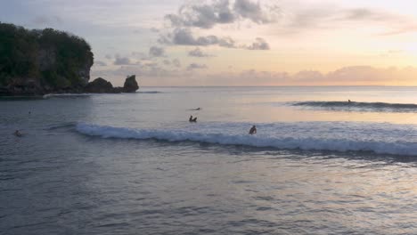 silhouetted surfers catching waves at sunset on padang padang beach, bali, indonesia