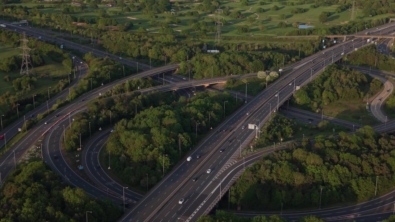 Una prospettiva aerea cattura un trafficato svincolo autostradale. Le auto guidano su più corsie e rampe, circondato da alberi verdi e campi.