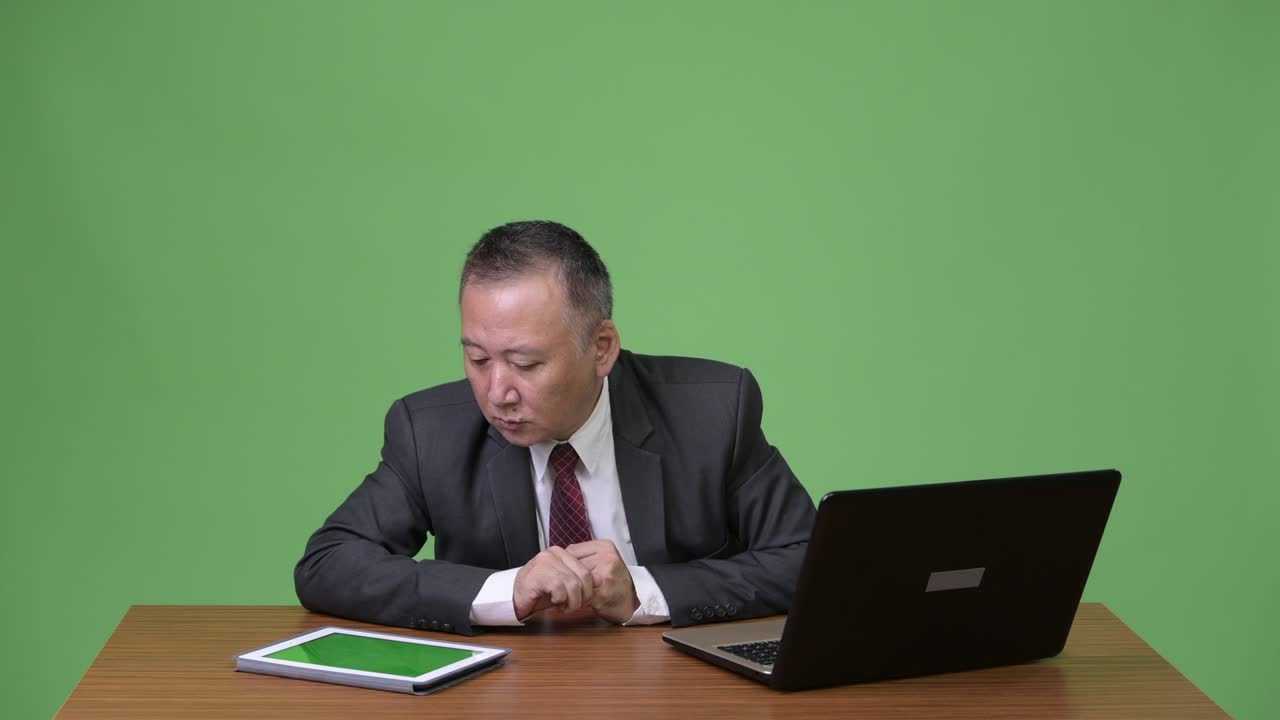 성숙한 일본인 사업가가 나쁜 소식을 듣고 두통을 고 있습니다.