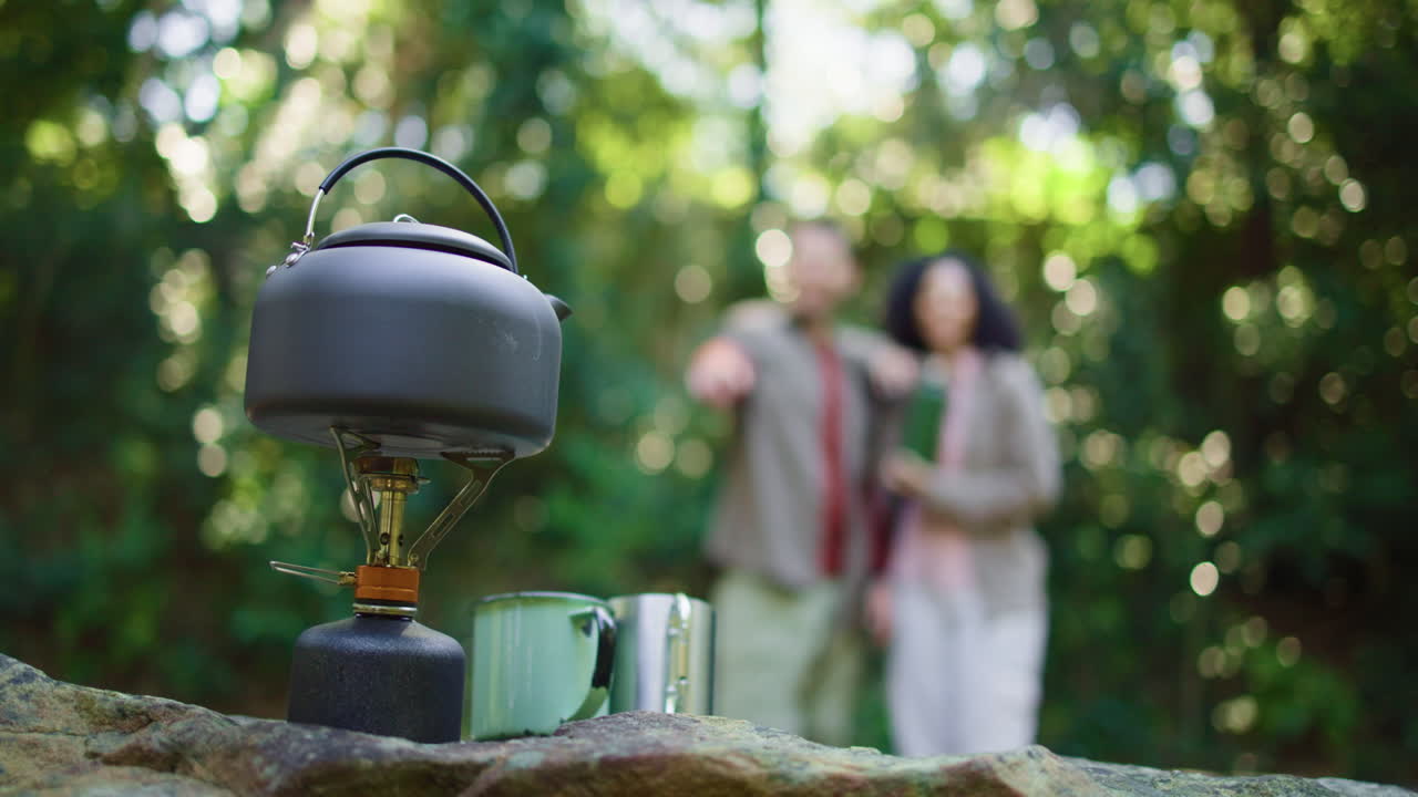 Camping scene with kettle, stove and couple in background