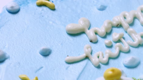 primer plano de la parte superior de un pastel de cumpleaños con glaseado azul y decorado con flores blancas y amarillas, con felicitaciones de cumpleaños en la parte superior