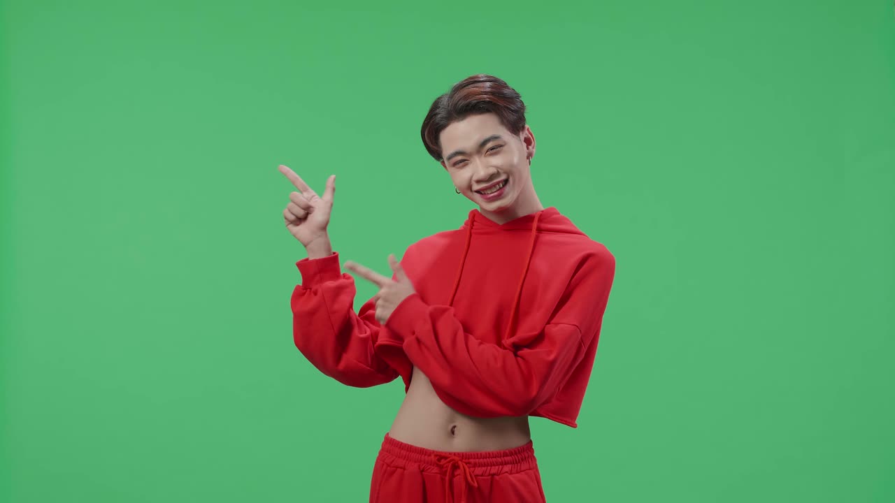 Den inspirerede asiatiske transkønnede mand smiler og peger til siden, mens han står i green screen-studiet.