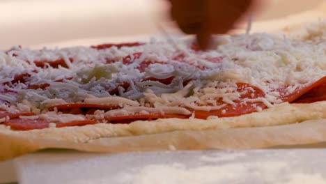 chef puts pepperonis and cheese on an uncooked pizza