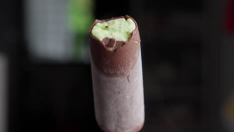 hand holding ice cream stick with chocolate and pistachio mint flavor, close up