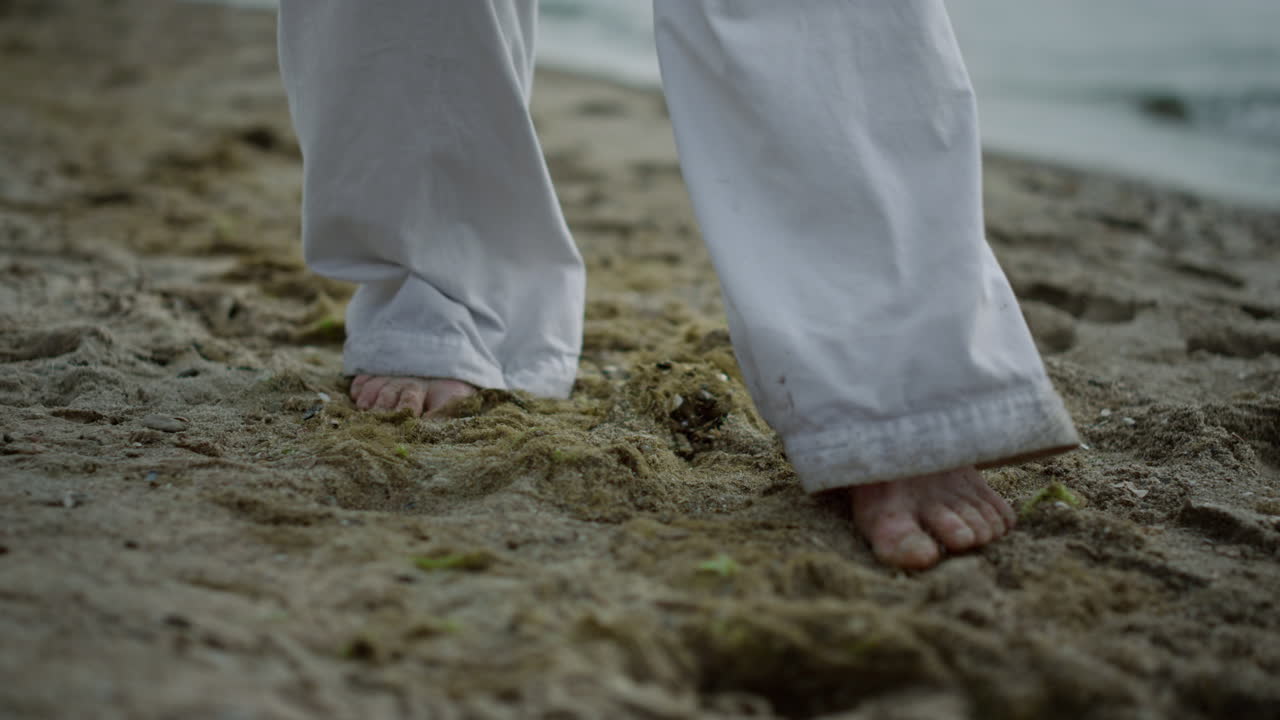Close-up pria tak dikenal tanpa alas kaki melangkah di pantai. Atlet berolahraga di pesisir.