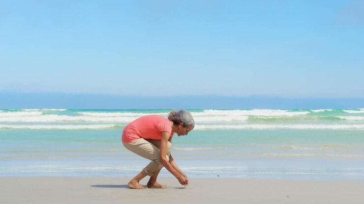 Side view of active senior African American woman picking up seashell on the beach 4k