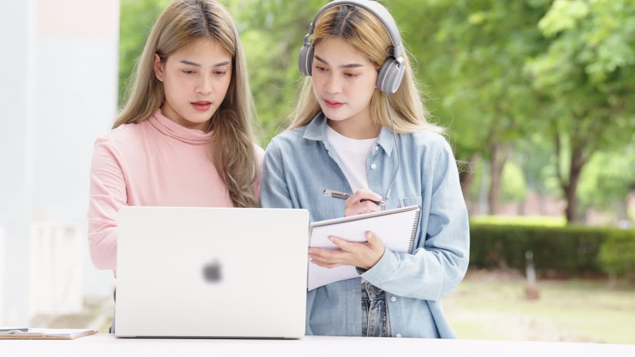Two Asian girls student partners are working on a laptop help study together