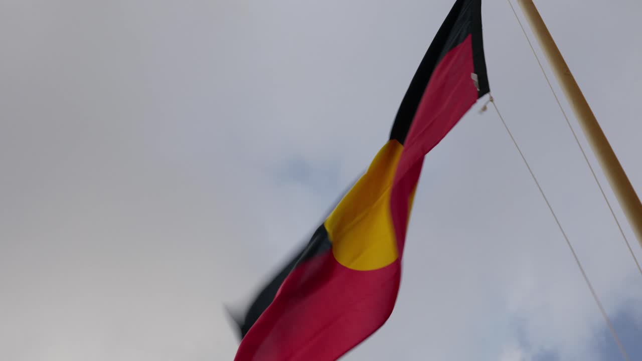 Bandiera aborigena australiana su un'asta in una giornata ventosa e nuvolosa.