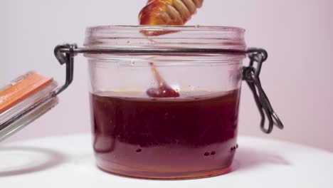 honey utensil dips in dark honey, drizzles, then sinks in glass jar, closeup