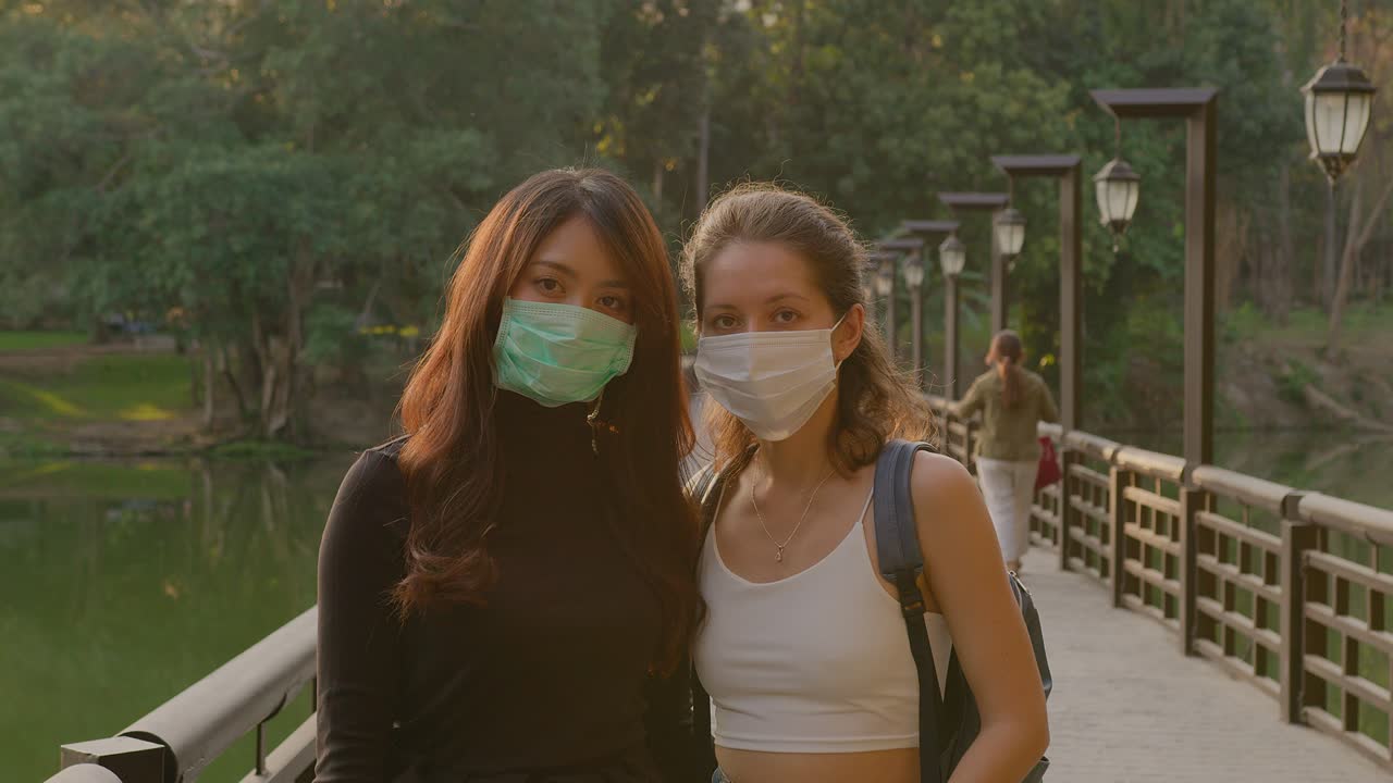 Two women wearing masks on a park bridge