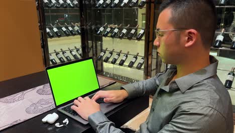 rich asian millennial entrepreneur typing on laptop with green screen inside luxurious home