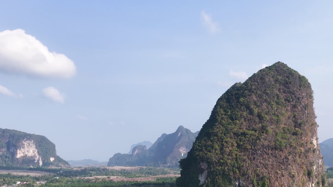 Ảnh chụp từ trên không bằng drone lia máy ngang qua những ngọn núi đá vôi nhiệt đới dưới bầu trời xanh trong.
