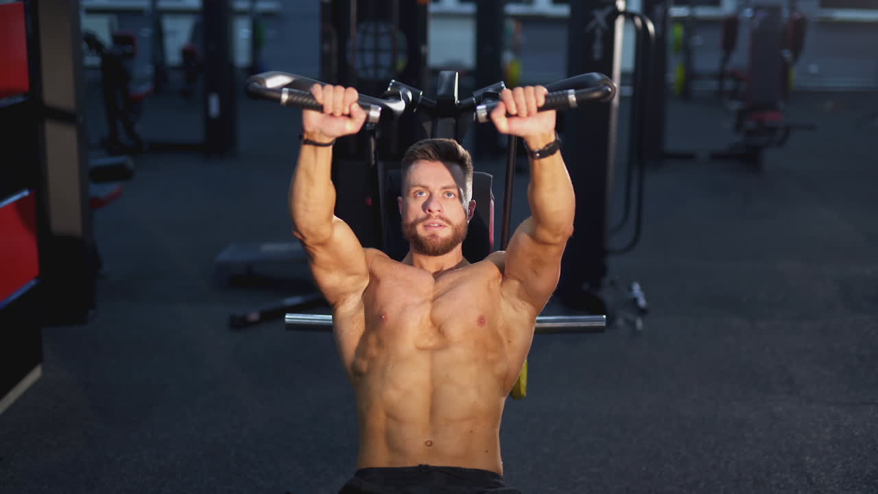 Muscular handsome man working hard in the gym. Bodybuilder with naked torso doing exercise.