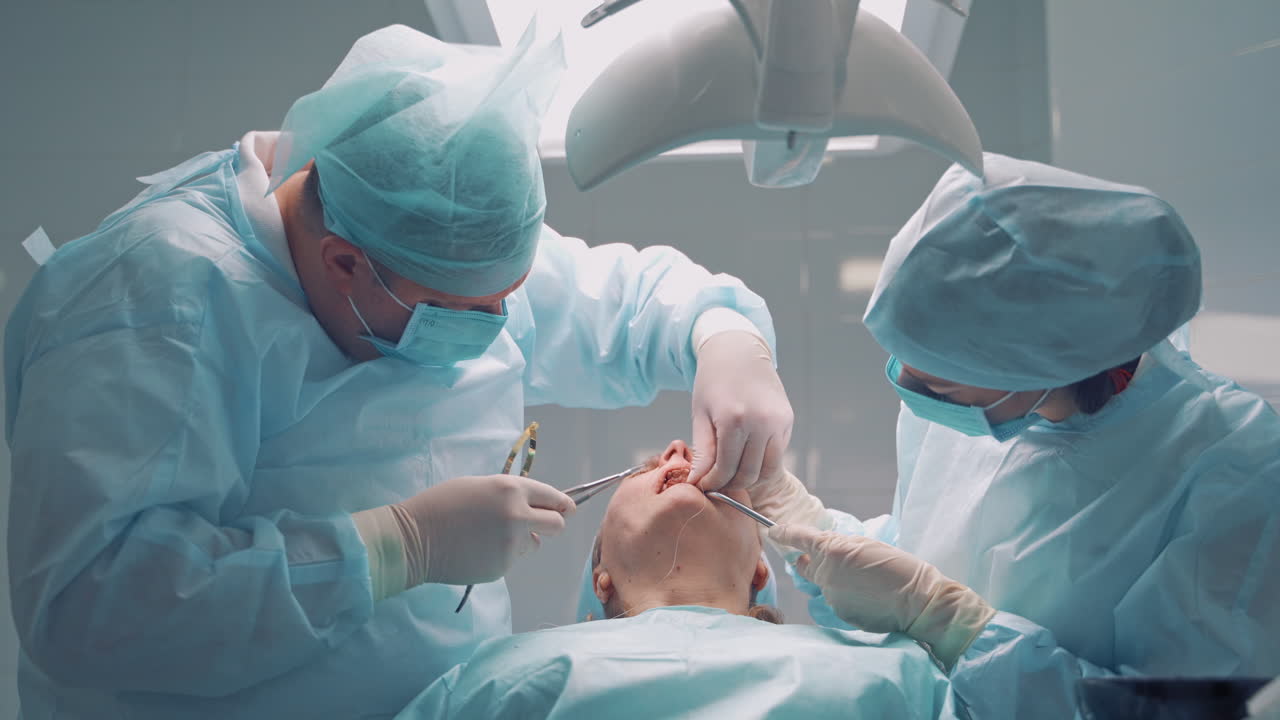 Dentist male works with a thread in patient's mouth in dental clinic. Specialist man and his assistant in medical uniform treat female's teeth in the stomatology center. Dental operation.