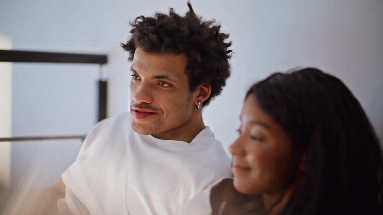 African american man drinking coffee lying bed with girlfriend. Lovers talking