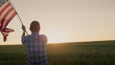 american farmer waving the us flag against the backdrop of a field of wheat where the sun rises