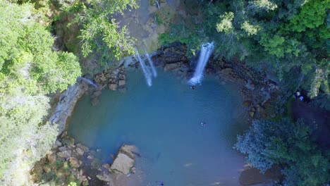 Vista-Aérea-Mientras-La-Cascada-Salto-Alto-Se-Sumerge-En-La-Piscina,-La-Gente-Nada