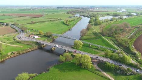 drone footage of english countryside featuring river bridge, infrastructure, sunny weather, and expansive rural farmland
