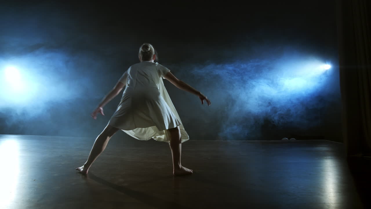 현대 발레 댄서 여성은 발바닥으로 스핀과 피루을 하고 무대에서 서서히 연기를 피우고 춤을 추고 있습니다.