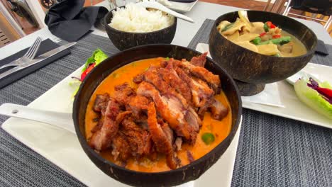 traditional thai red curry crispy duck dish and green curry chicken with rice in coconut bowls, tasty thai cuisine restaurant, 4k shot