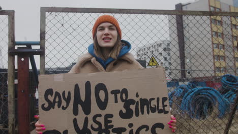 young female activist holding a cardboard placard and protesting to save the earth during a climate change protest while looking at camera