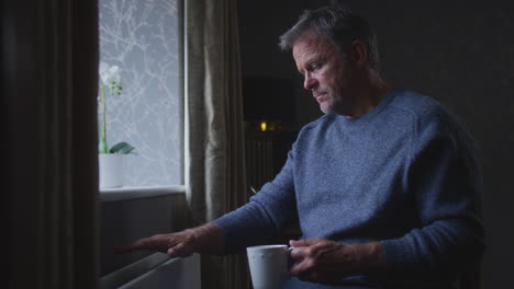 unhappy mature man trying to keep warm by radiator at home during cost of living energy crisis