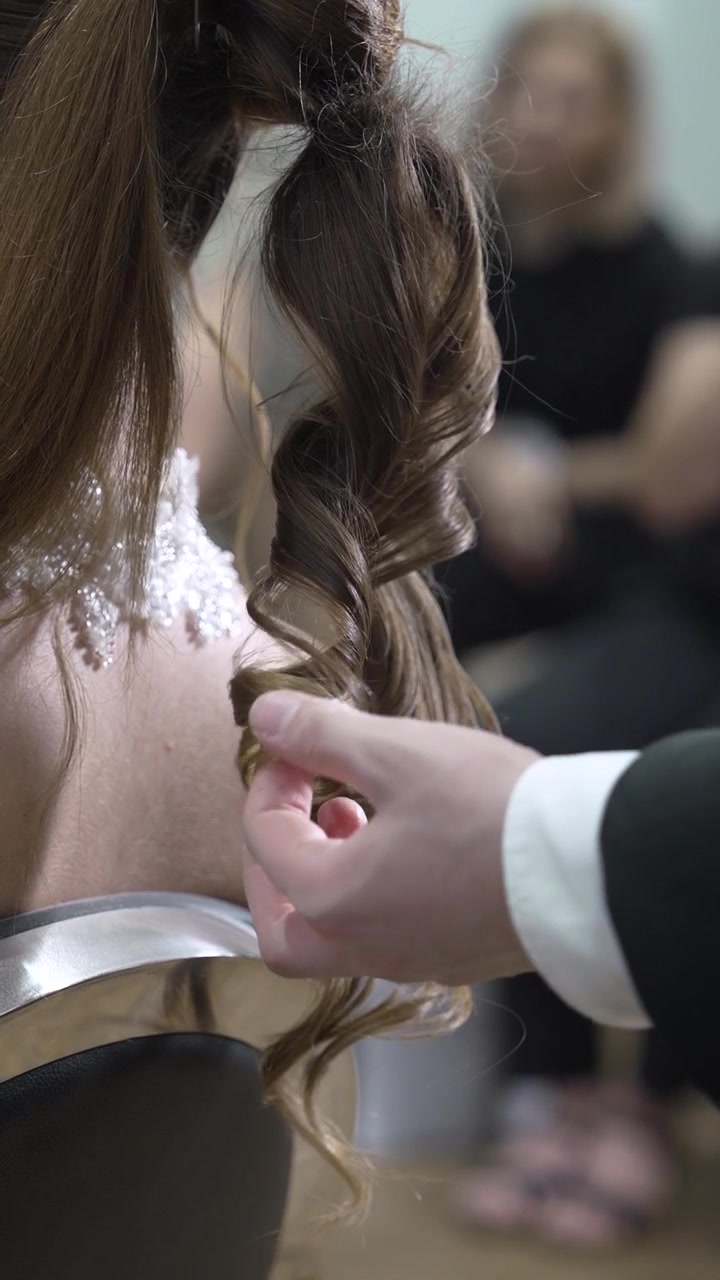 Uno sposo aiuta la sua sposa con l'abito da sposa in una stanza vivace piena di invitati. Condividono un momento speciale prima dell'inizio della cerimonia, mostrando il loro amore e la loro connessione.