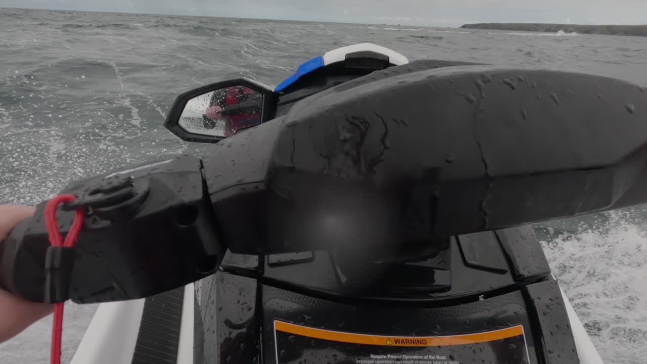 Rekaman POV seorang pengendara jet ski yang melaju melintasi ombak besar di laut dan terkena cipratan air.
