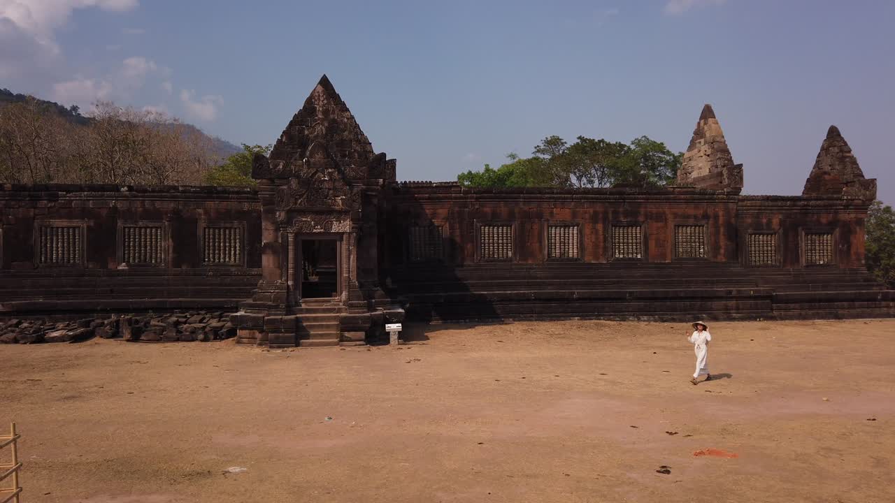 Young beautiful woman traveler in long white dress and vietnamese hat walking near Khmer palace in Wat Phou ruined Hindu Temple complex. Champassak, Laos, Asia. Ancient culture religious architecture.