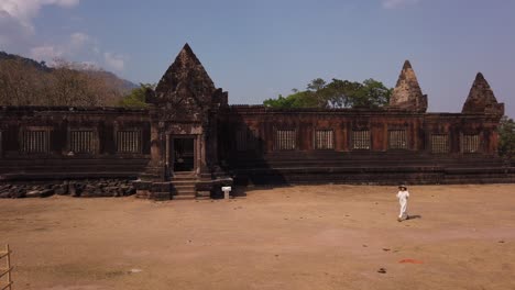 young beautiful woman traveler in long white dress and vietnamese hat walking near khmer palace in wat phou ruined hindu temple complex. champassak, laos, asia. ancient culture religious architecture.