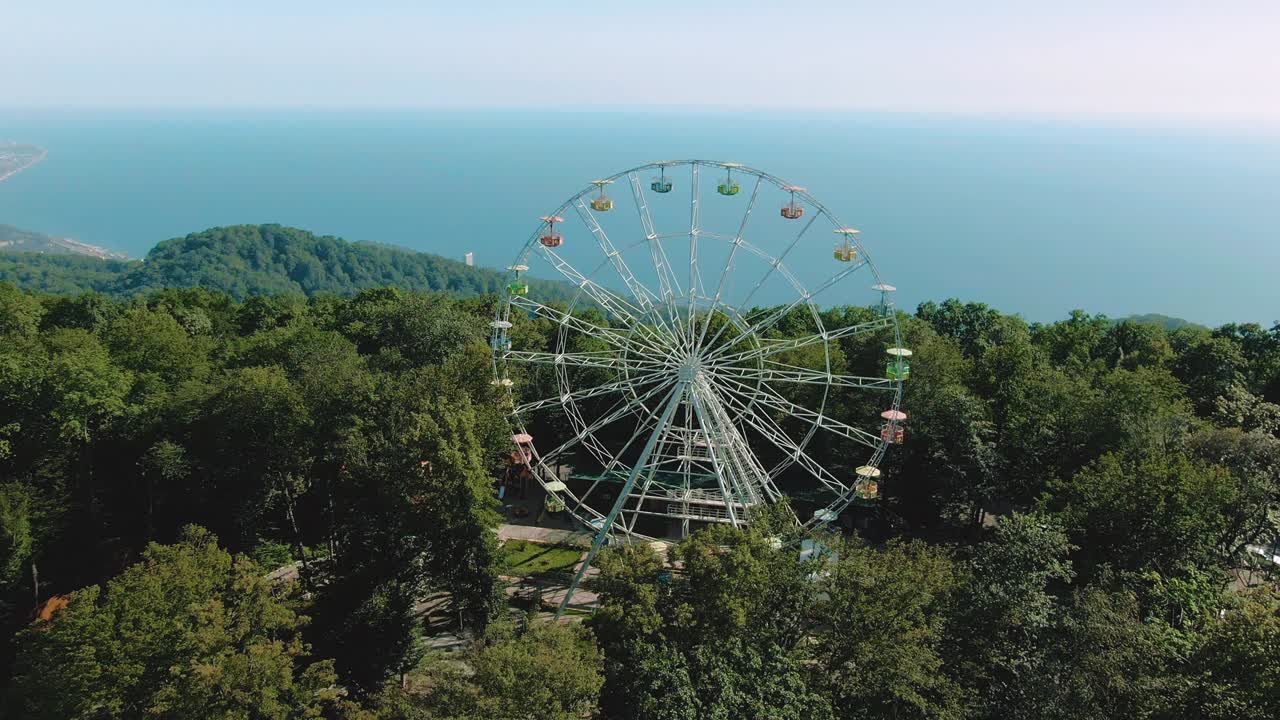 vista aérea de 4k. una rueda de ferris gira en la cima de una montaña. impresionantes vistas de las montañas y el mar. atracción para adultos y niños