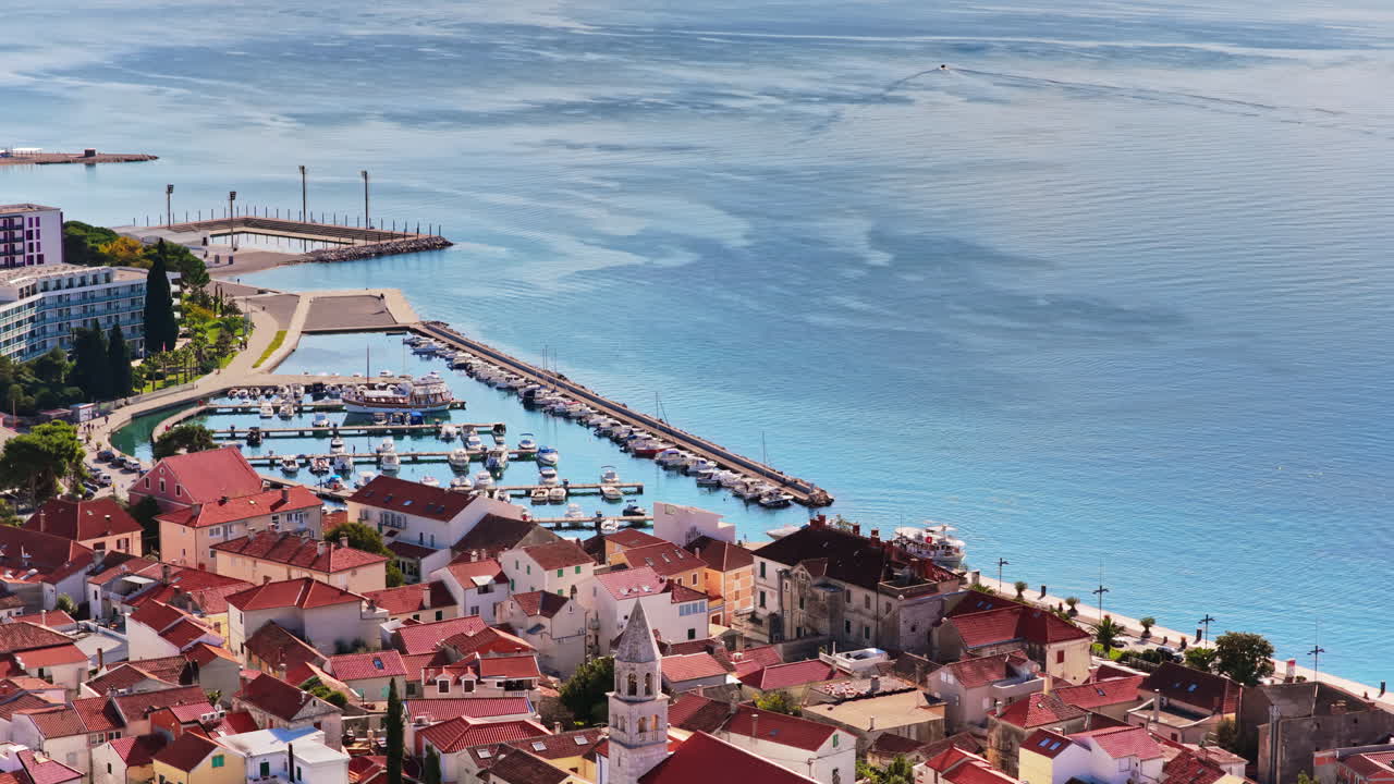 Aerial drone view of Biograd's residential area near the marina, showing clusters of red roofed homes with the harbor and anchored boats visible in the background. Biograd na Moru, Croatia