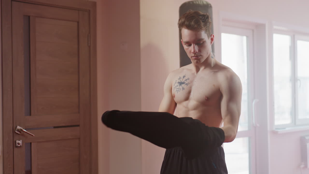 Soldier in black long sleeve shirt standing as he took off his top in gym environment with focused expression, as he takes off his shirt looking sideways with arms crossed, showing neck tattoo