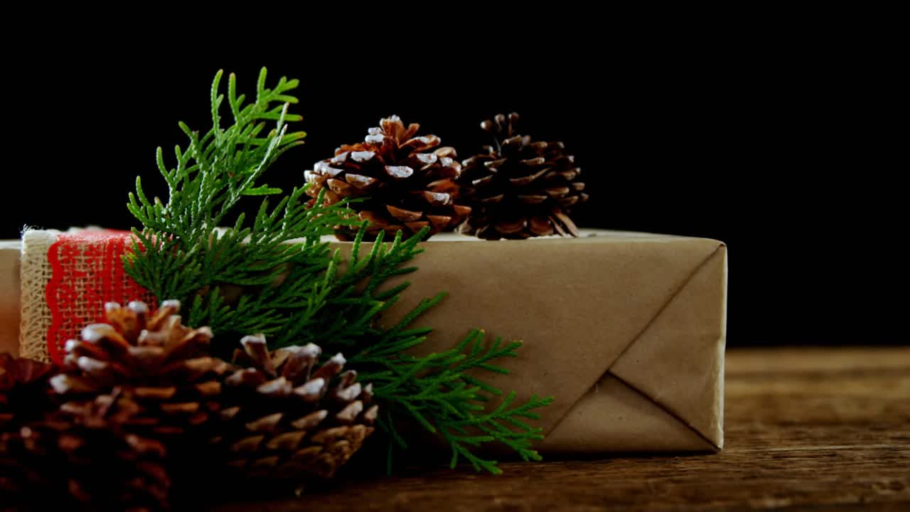 Hand adding candle beside gift and pine cones, sparkles drifting, lighting and removing making glow