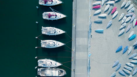 White-sail-boat-and-yachts-docked-by-pier-with-sunfish-boats-on-sand