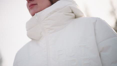 free spirit girl zipping winter coat on breezy winter day with gloved hands moving zipper upward toward collar while cold wind tousles hair and winter sun glints off glossy fabric smile