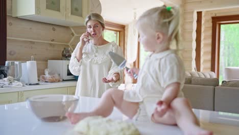 mother talking on phone while daughter plays in the kitchen