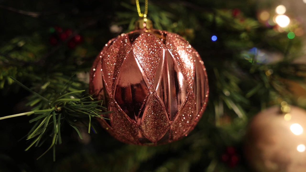 Toma lenta de travelling hacia una bola rosa brillante colgando de un árbol de Navidad