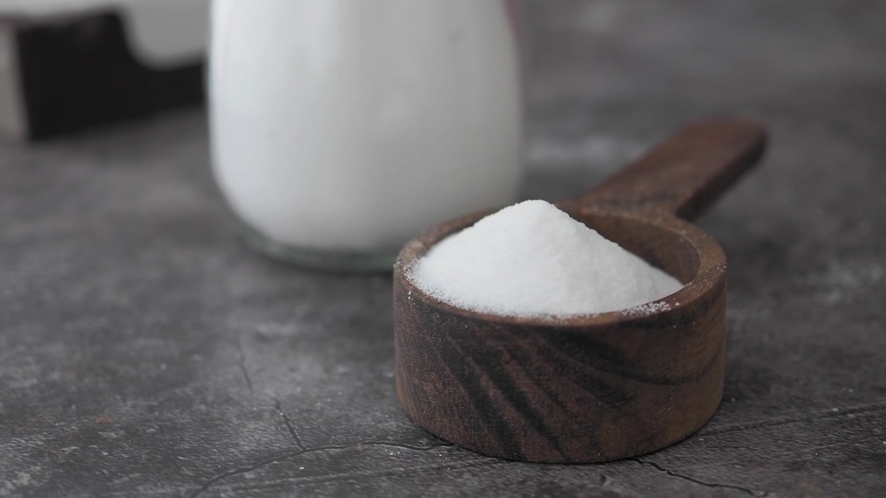 Açúcar Branco em uma Colher de Medida de Madeira sobre uma Superfície Escura